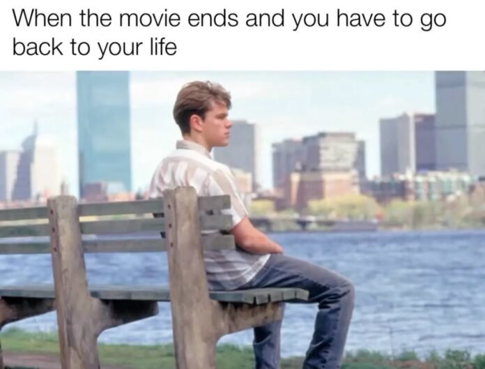 A person sits alone on a bench facing a city skyline with text joking about the sadness of returning to reality after finishing a great movie.