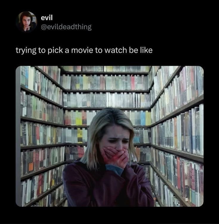 A person looks overwhelmed while surrounded by rows of movie cases, humorously representing how difficult it is to choose something to watch.